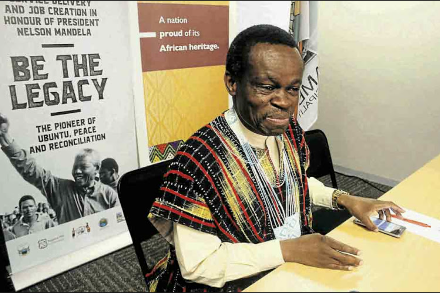 PLO Lumumba in African attire seated before Nelson Mandela legacy banners